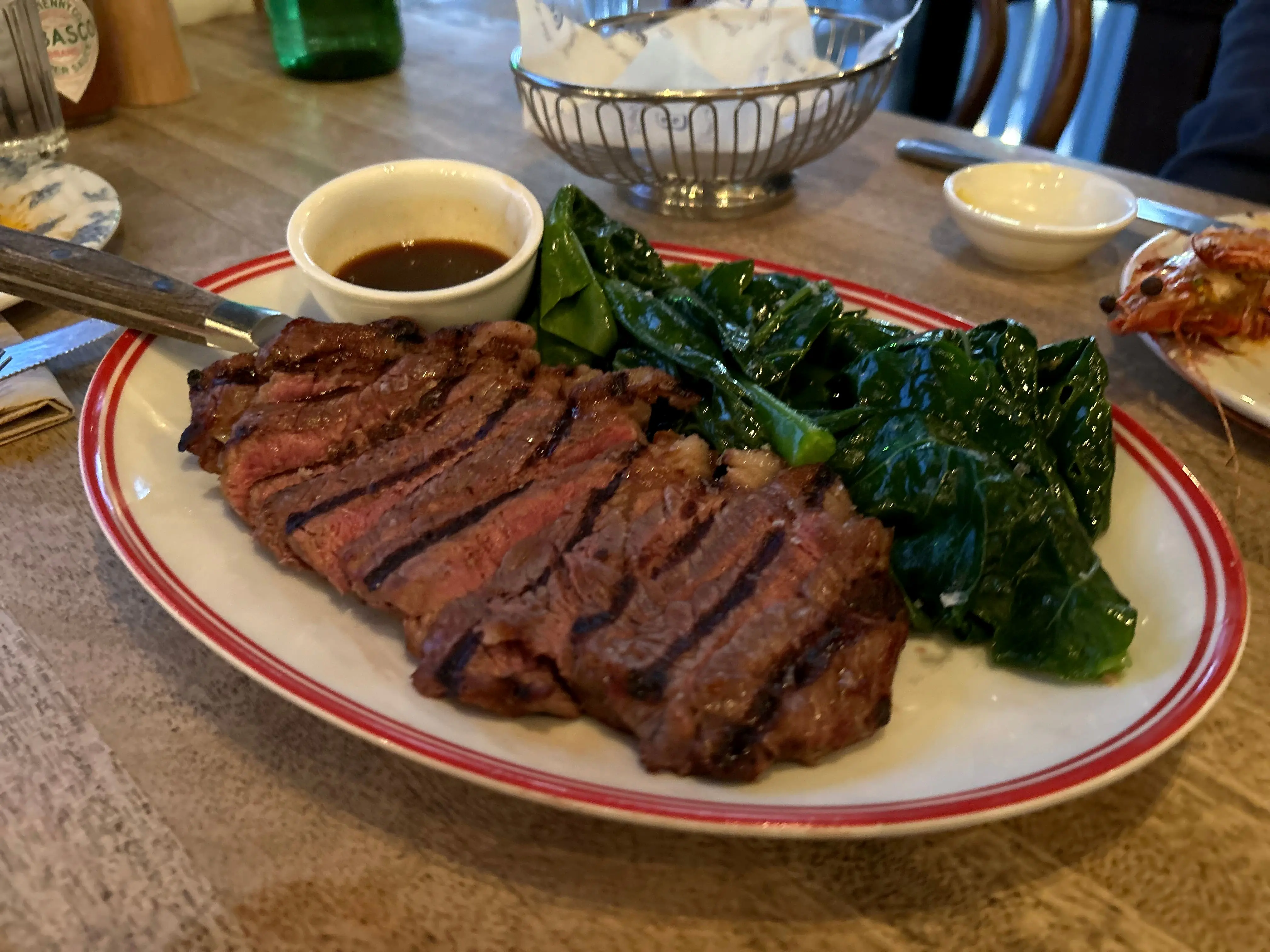 A sliced grilled steak with greens and jus on a red-rimmed plate at Balcony Bar