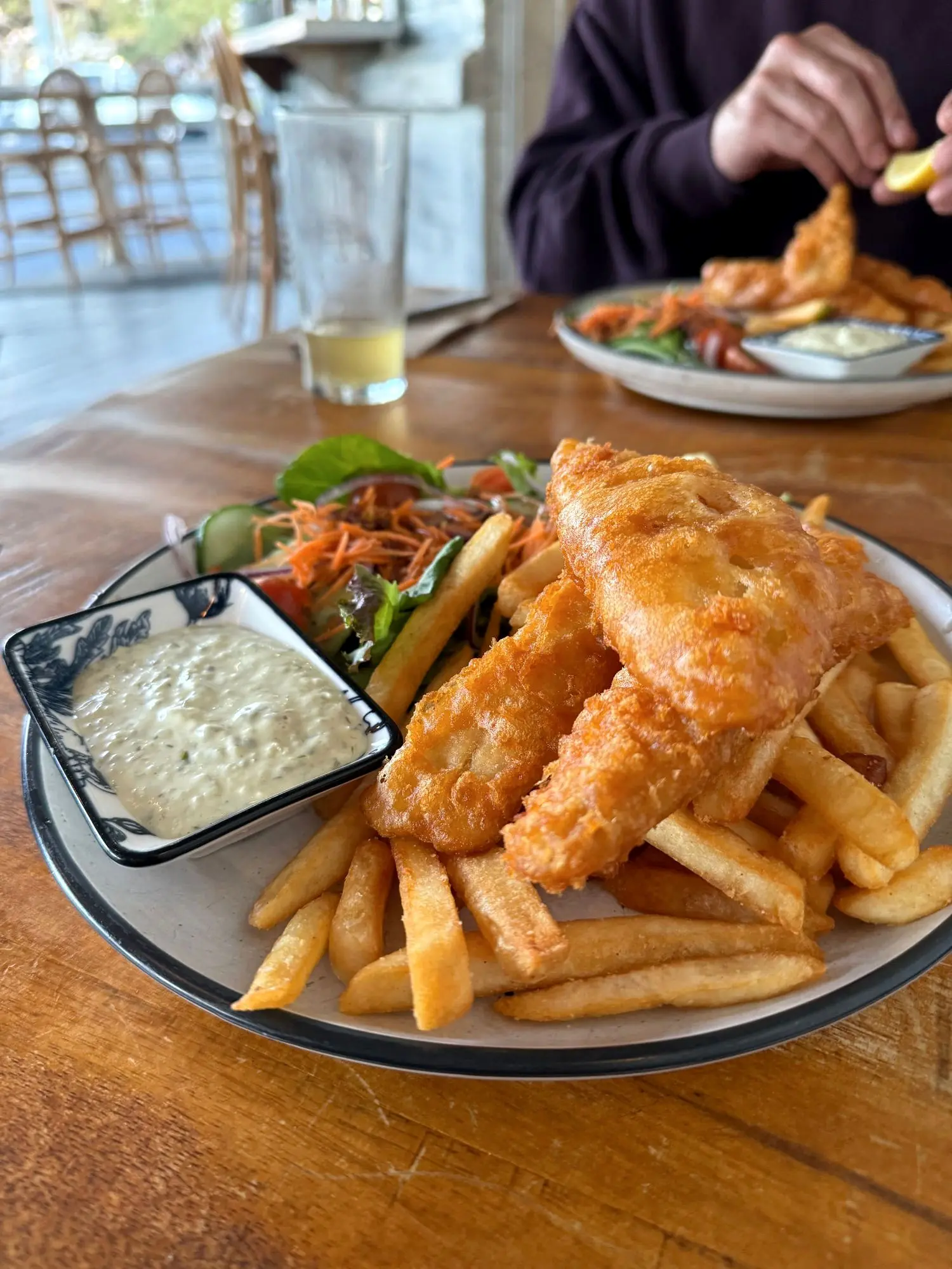 Beer-battered fish with golden chips, salad and tartare on a plate at a Byron Bay table