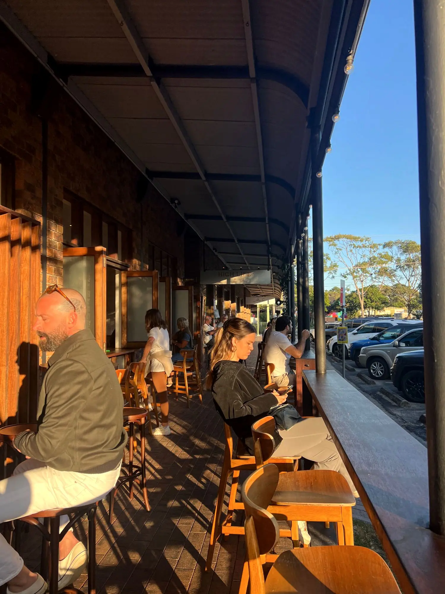 The open-air Highlife rooftop terrace at golden hour — diners at timber tables under festoon lights, looking out over the street