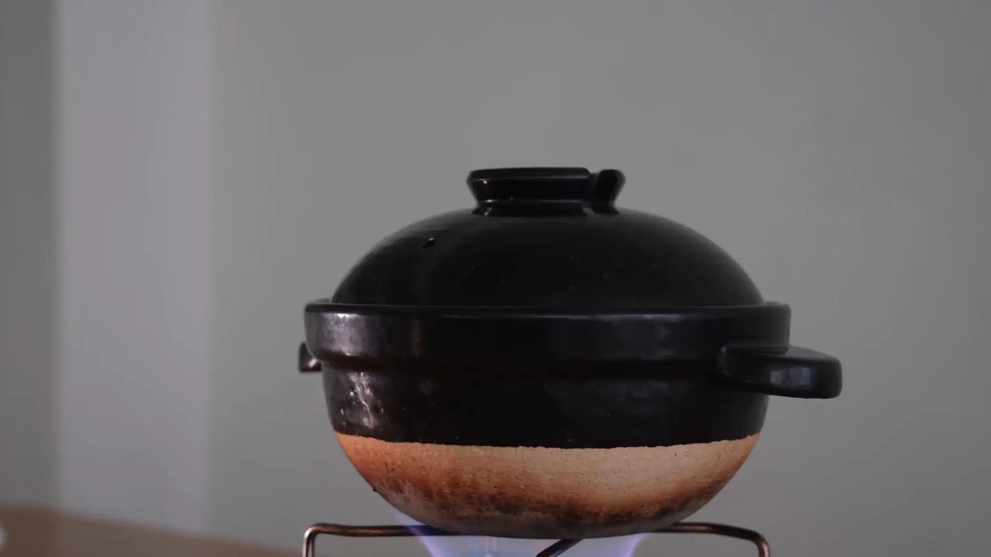 A black clay donabe pot with a scorched base sitting over a blue gas flame