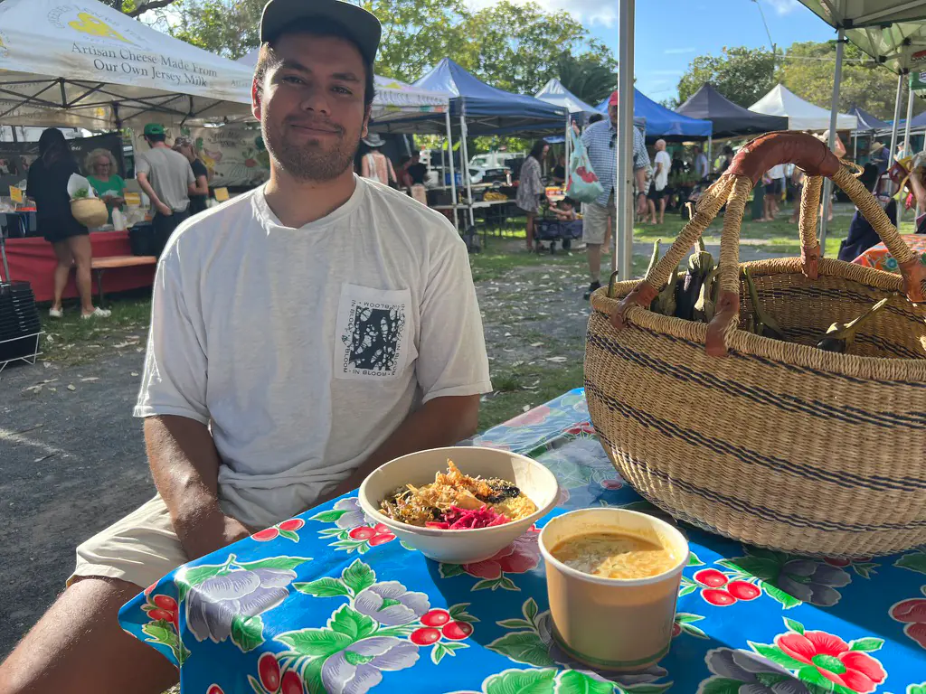 A Japanese breakfast donburi rice bowl with a cup of miso soup and a woven basket of eggplant on a market table at the Byron Bay Farmers Market