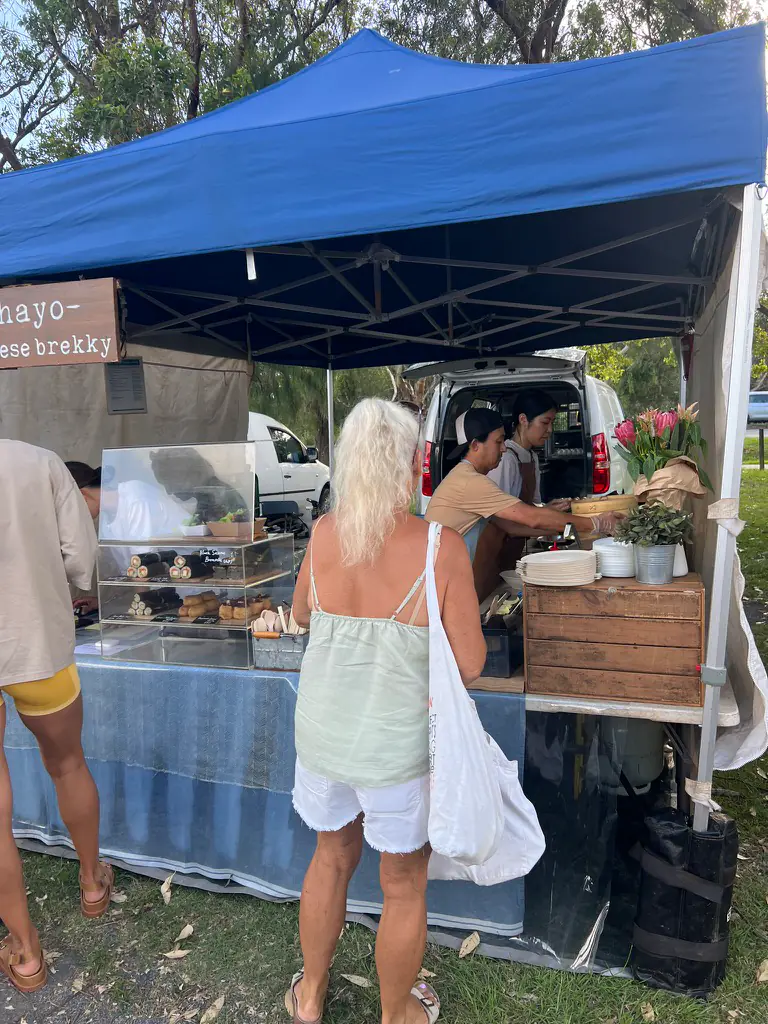 The Ohayo Japanese Brekky stall by Ebiya at the Byron Bay Farmers Market, with a cabinet of food, proteas and customers ordering at the van