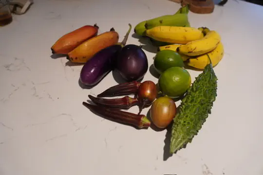 A spread of market produce on a bench — finger bananas, Japanese eggplant, red okra, bitter melon and limes from the Byron Bay Farmers Market