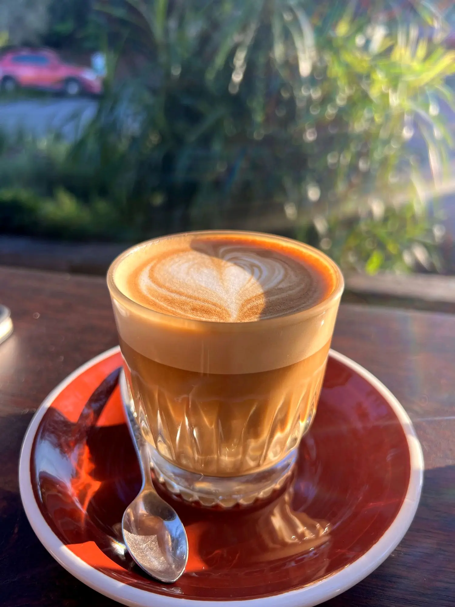 A glass of coffee with latte art on a red saucer in golden afternoon light at Highlife Byron Bay