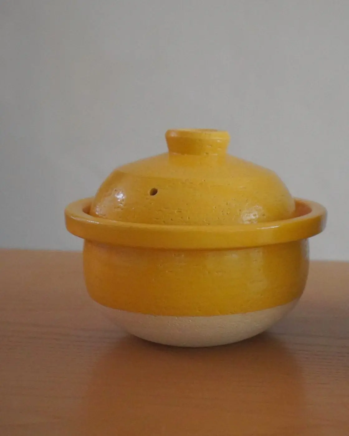 The mustard Matsusho donabe on a wooden table against a plain wall.