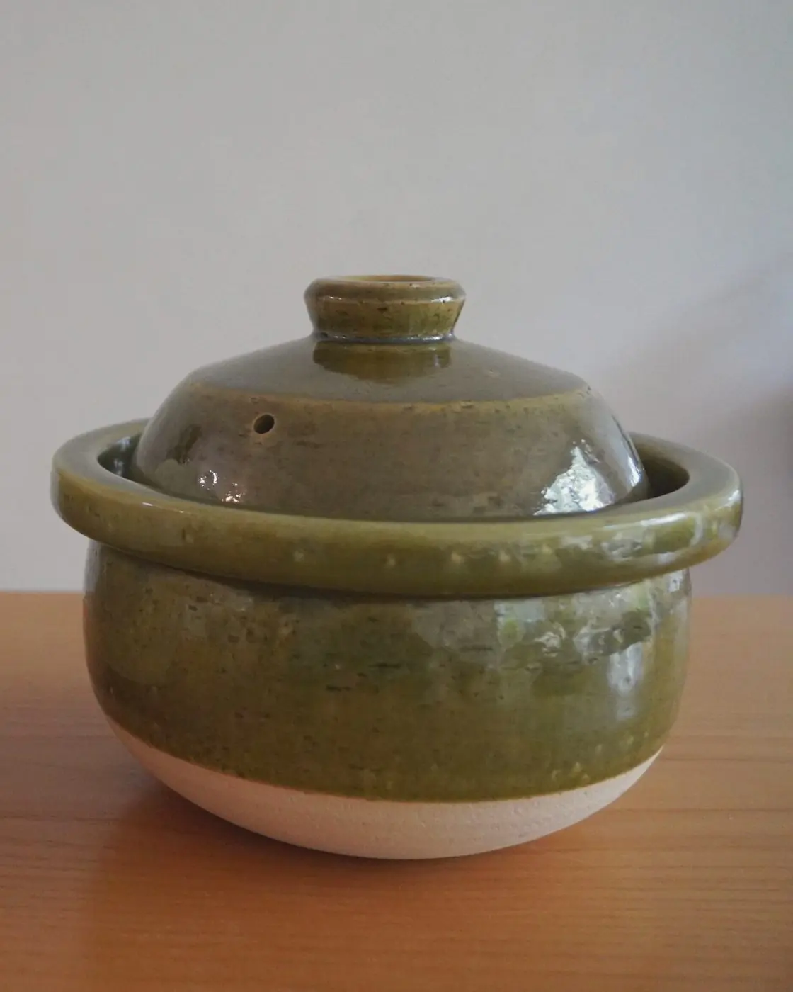 The olive Matsusho donabe on a wooden table against a plain wall.