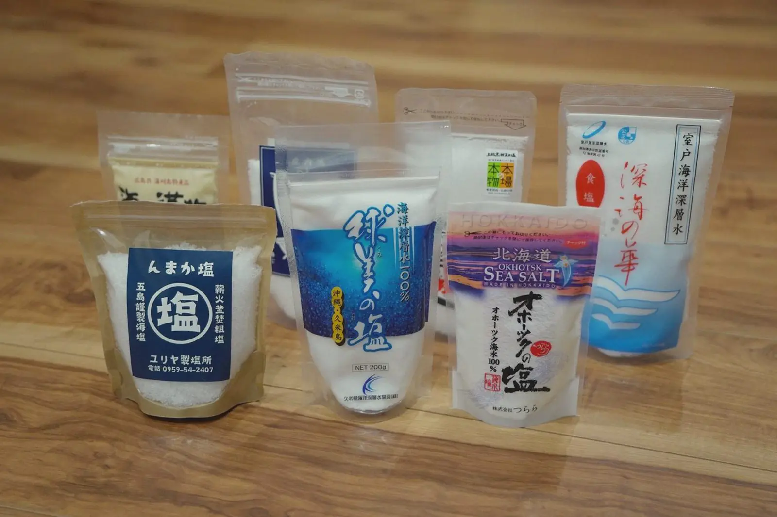 Seven bags of Japanese sea salt from different regions lined up on a wooden floor.