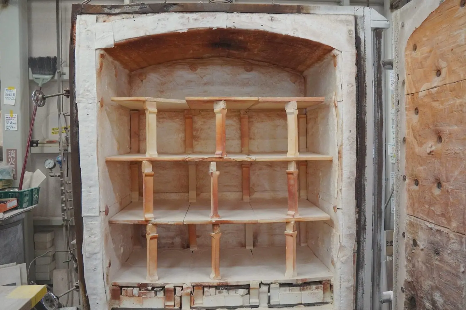 The open door of a kiln, showing shelves and clay posts inside.