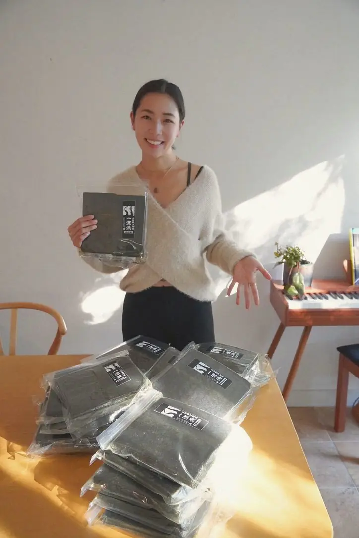 Tomoyo, owner of Pocket Rice, holding up a pack of Ichiryūhama nori beside a table stacked with more packs.