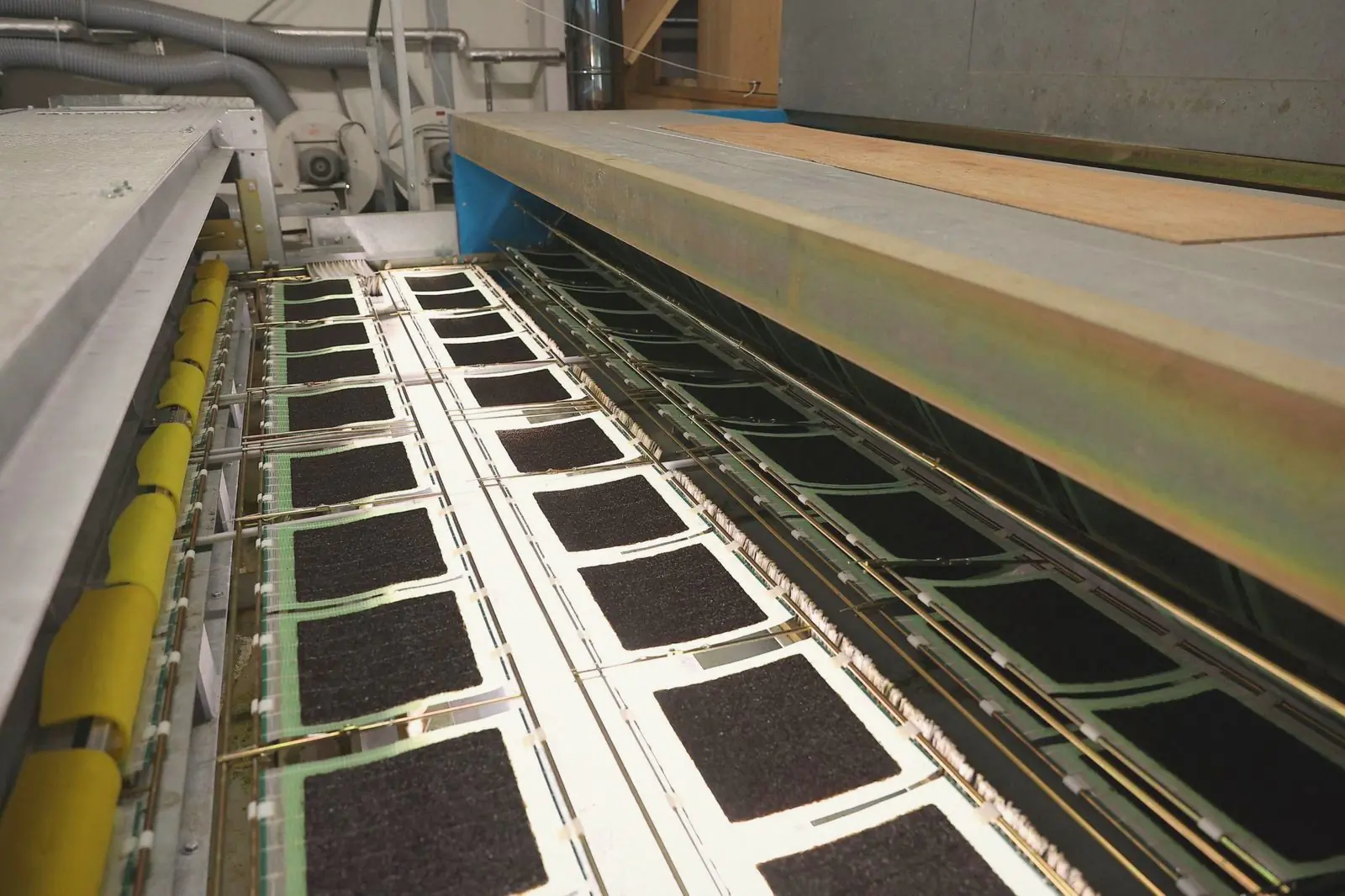 Rows of square nori sheets on frames moving through a drying machine.