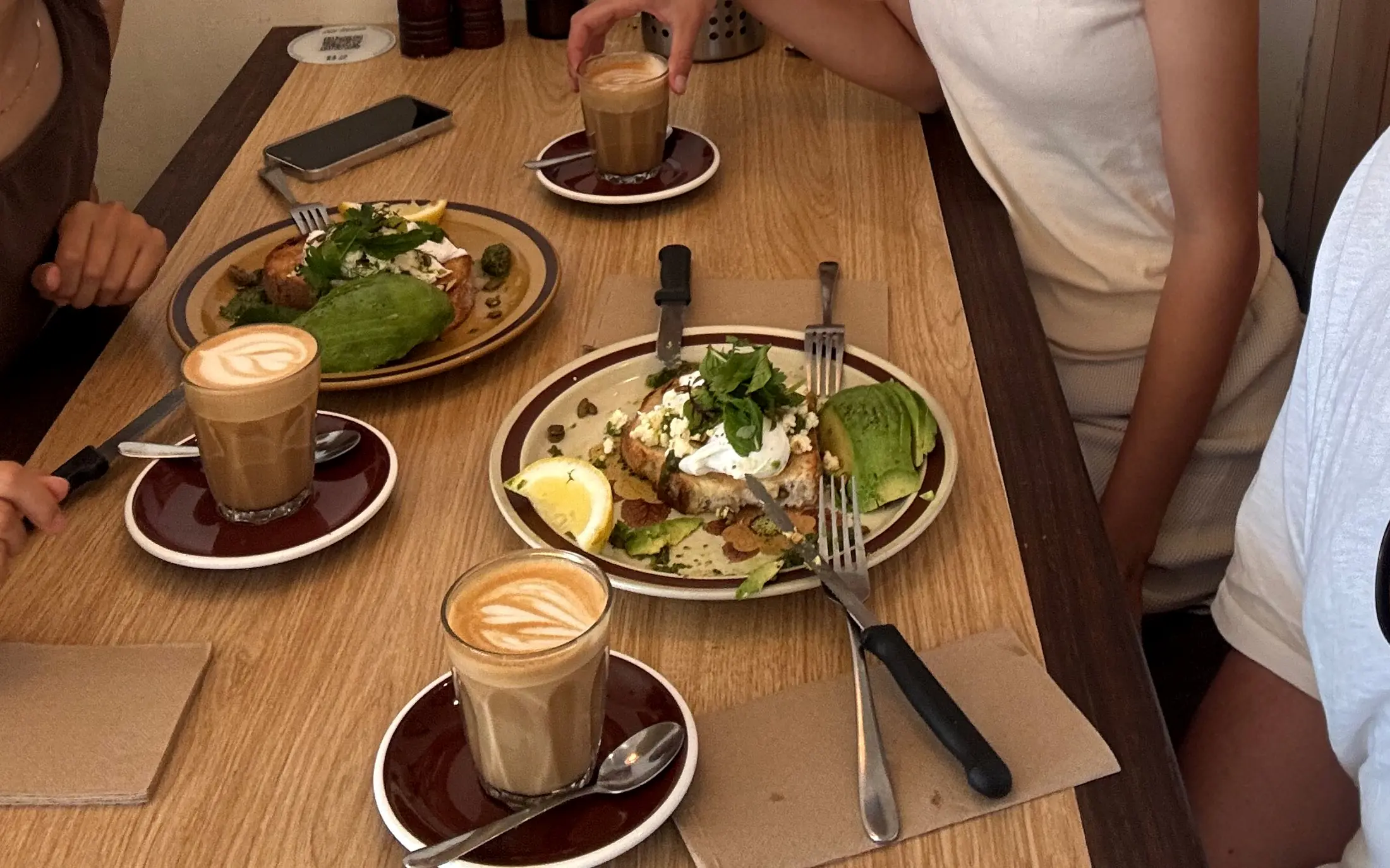 A table of brunch at Old Maids — avocado on toast, poached eggs and three lattes on a timber table