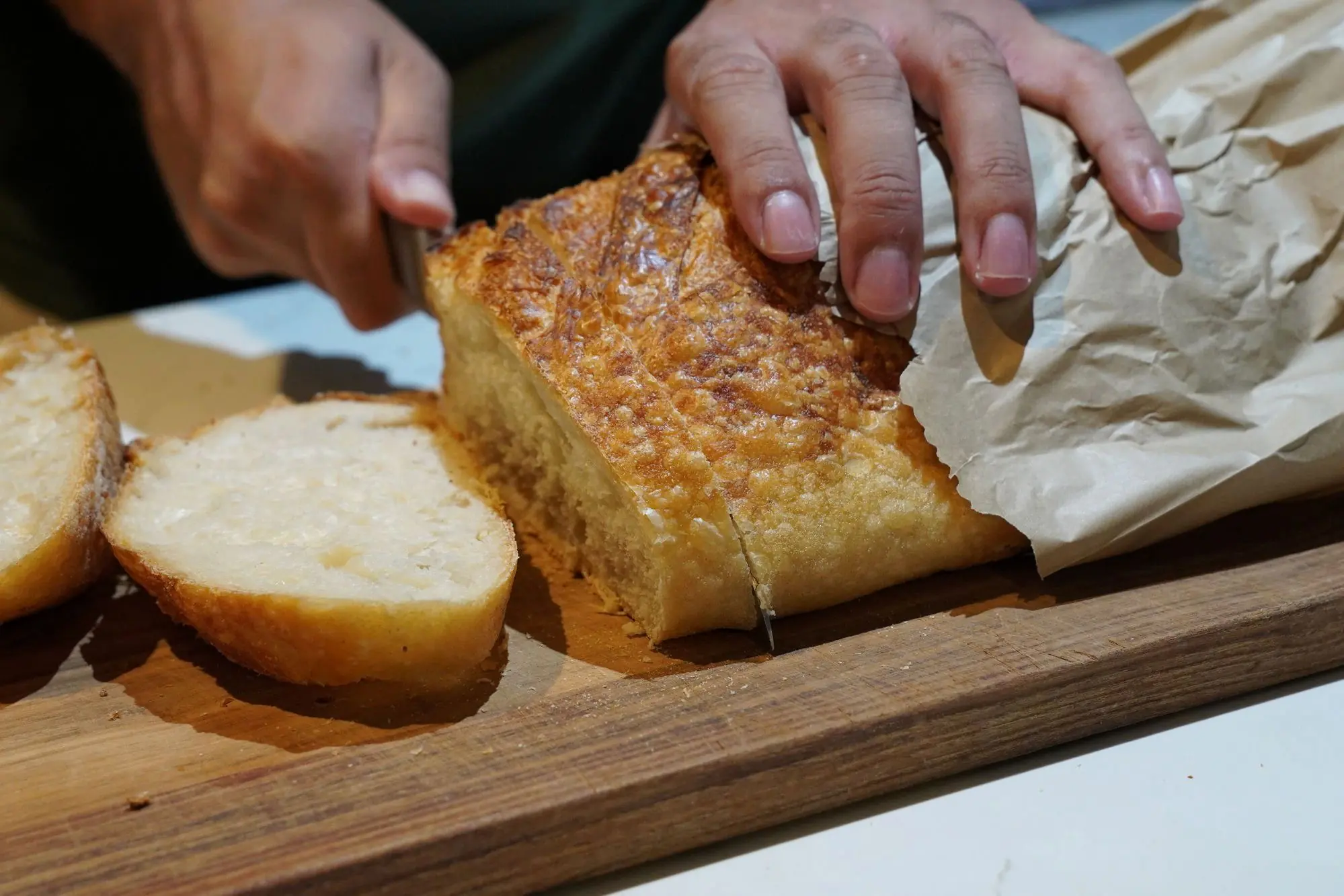 Hands slicing into a crusty sourdough loaf, showing the soft open crumb, at Sunday Sustainable Bakery