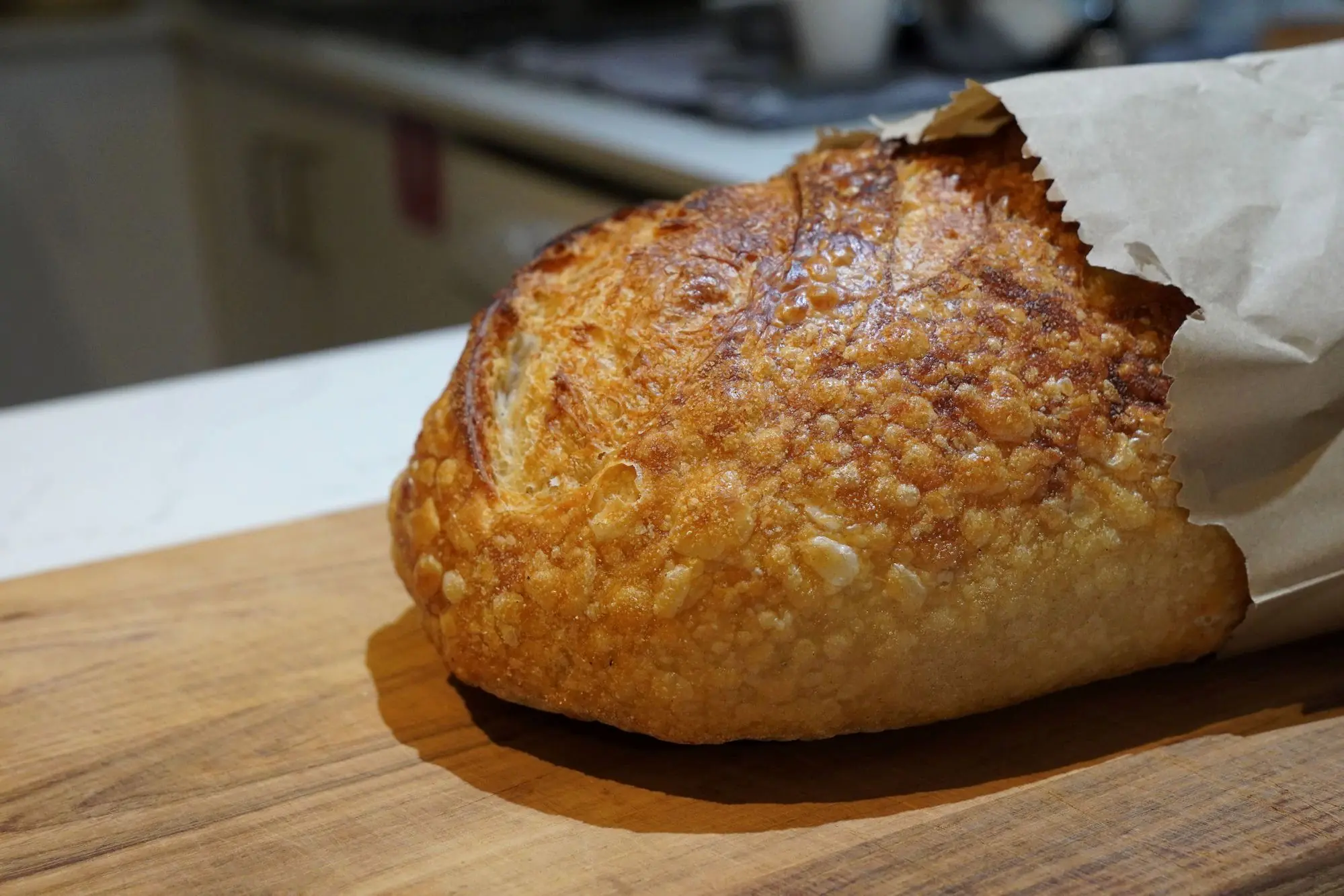 A golden, crusty sourdough loaf in a paper bag on a wooden board at Sunday Sustainable Bakery